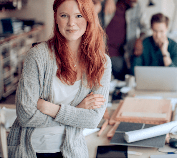 Young woman with long red hair and mild rosacea, smiling at the camera lens with her arms crossed. Not an actual patient.